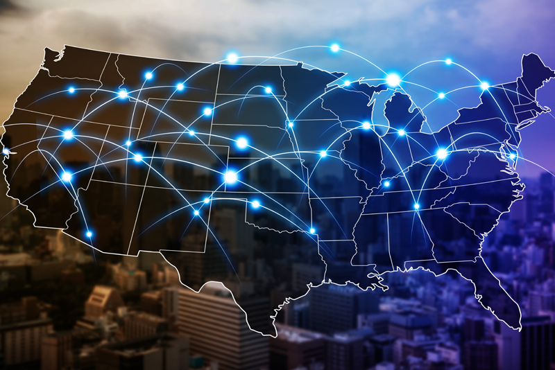 A digital overlay map of the United States featuring interconnected white lines and glowing blue nodes spread across the country over a blurred city skyline.